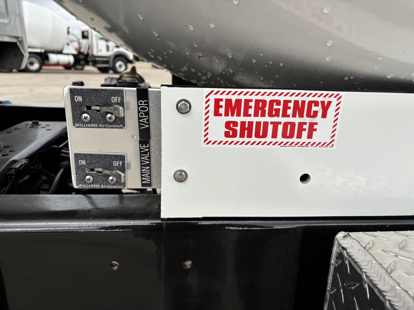 Emergency shutoff switch and control levers on Mack MD7 component visible in engine area with label EMERGENCY SHUTOFF and MAN VALVE/VAPOR text.