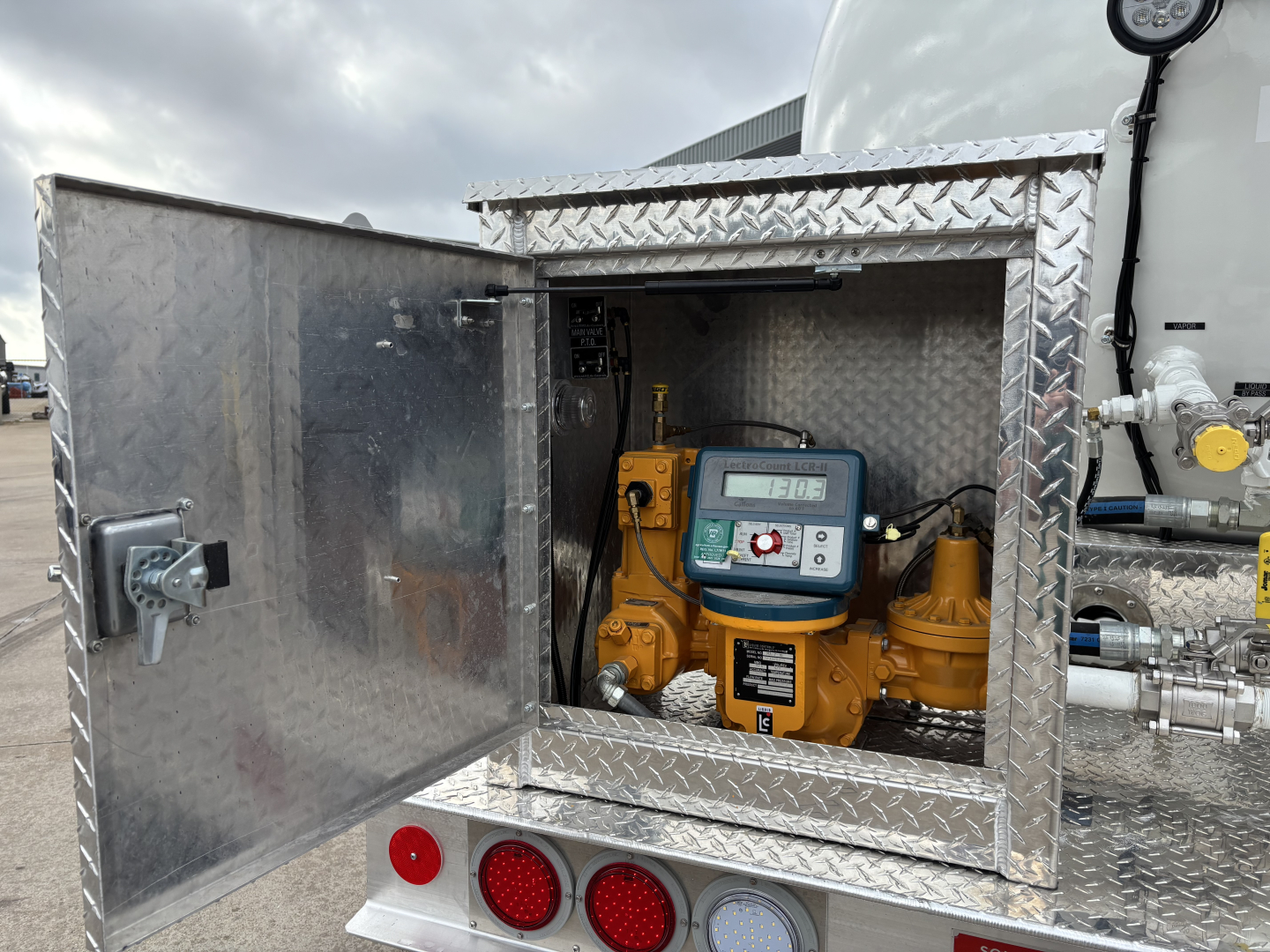 Open diamond-plate access panel showing a yellow gas engine starter and control panel inside a utility box on a Mack MD7 truck engine bay.
