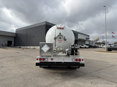 Rear view of a Mack MD7 tractor with a large cylindrical tank trailer attached, in a dealership lot.