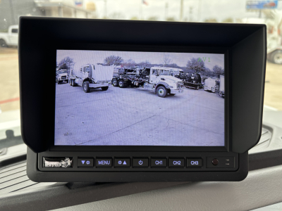 In-vehicle color display monitor with control buttons in front; screen shows a parking lot with trucks. Visible text on unit includes 'Bus' or 'Buyer' label on lower left and buttons labeled MENU, CH1, CH2, CH3. No other legible text clearl