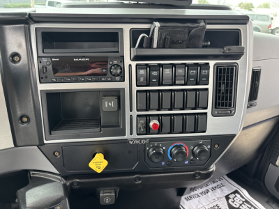 Dashboard panel of a 2026 Mack MD7 truck showing radio, switches, climate controls, and a yellow hazard sticker.