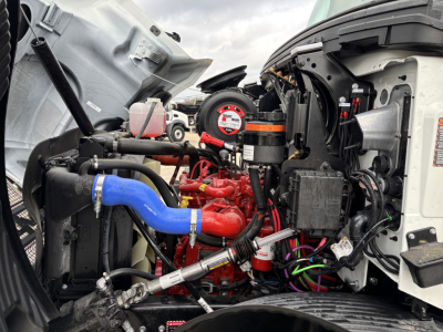 Mack MD7 engine bay showing red engine block, blue intake hose, various hoses, wiring, and front cab components.