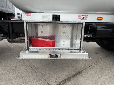 Truck side view showing a diamond plate storage compartment under the fuel tank with a red toolbox inside and steps. emergency labels visible.