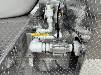 Machinery valve assembly and piping in a diamond-plate engine bay with a yellow-handled valve and inline fittings.