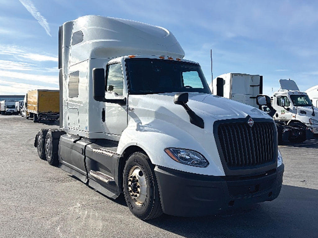 Truck cab interior not visible; white 2023 International LT625 sleeper tractor in a parking lot, front-left angle showing grille, headlights, and side mirrors.