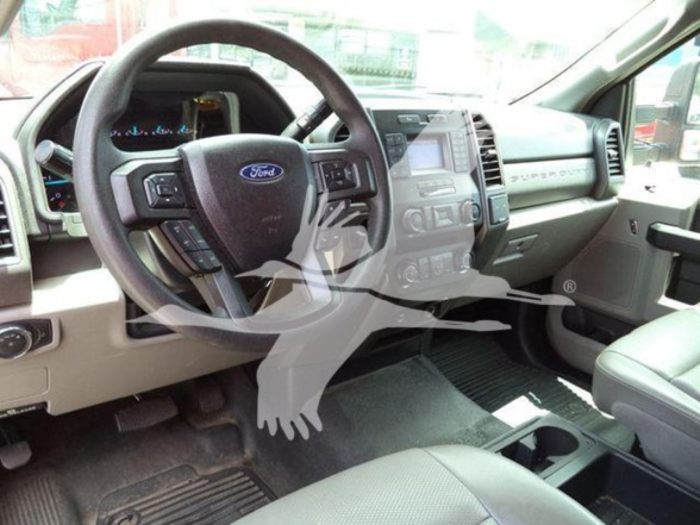 Ford F-550 interior driver area showing steering wheel with Ford emblem, center console, dashboard, and beige seats in a used truck.