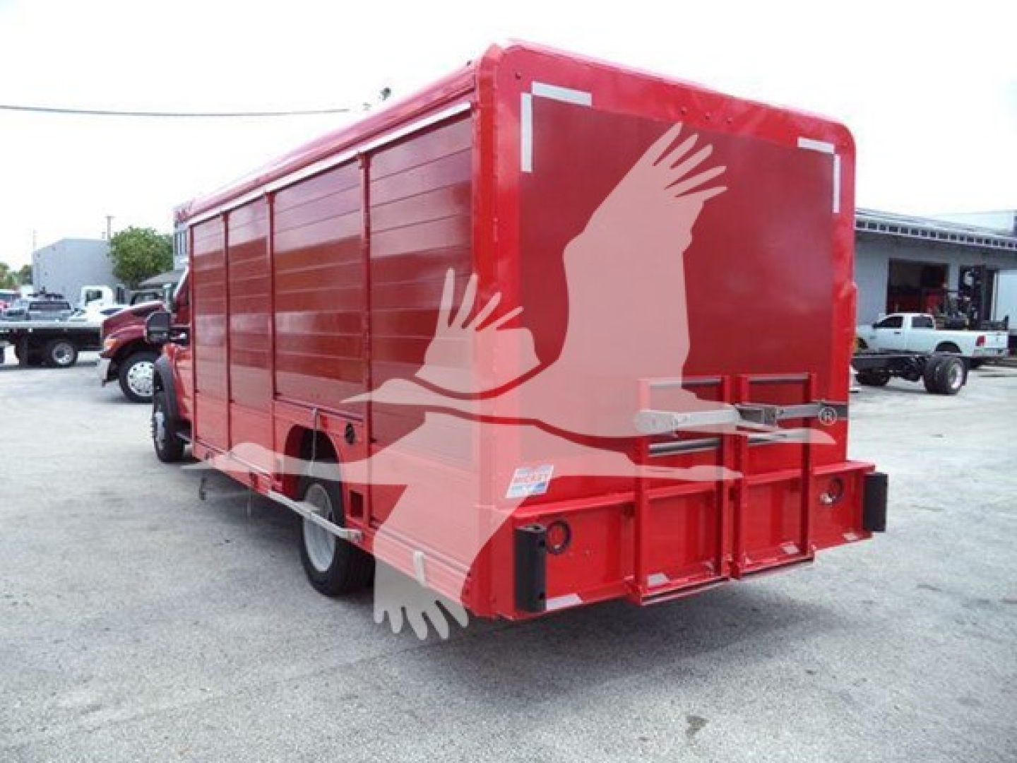 Red Ford F-550 box truck rear view with open rear doors and reflection of surroundings.