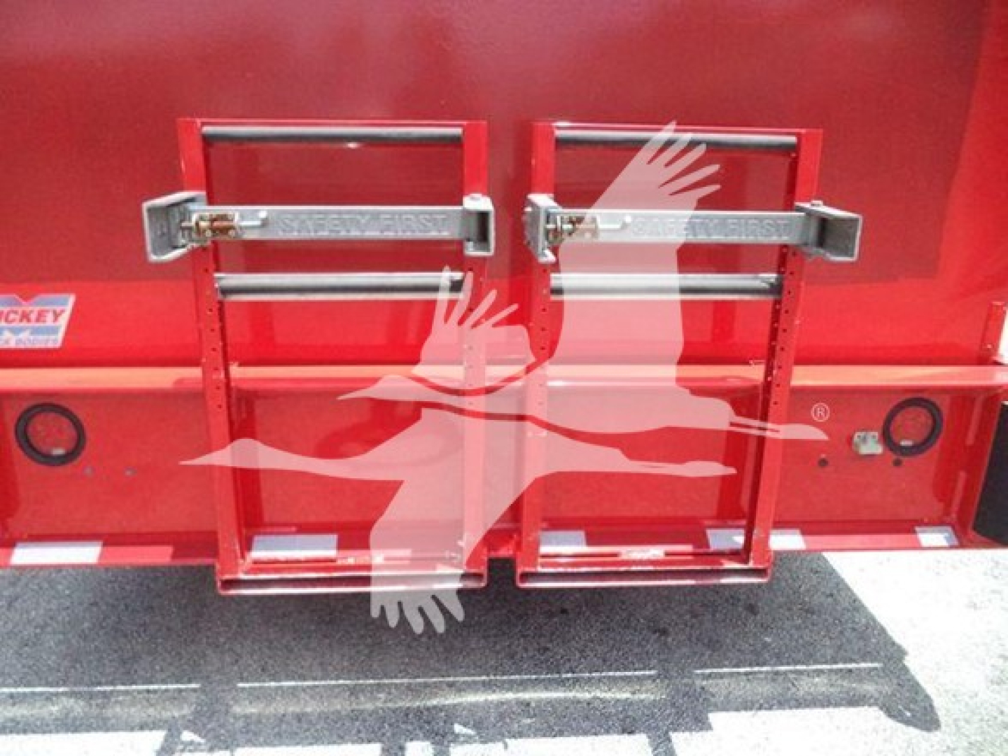 Rear view of a red Ford F-550 stake truck body with dual step panels and safety latches, showing a graphic bird watermark and stabilizer mounts.