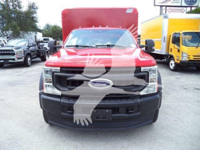 Front view of a red 2020 Ford F-550 truck with black grille and bumper, F-350-like headlight assembly visible, Ford emblem on grille. Other trucks parked nearby.