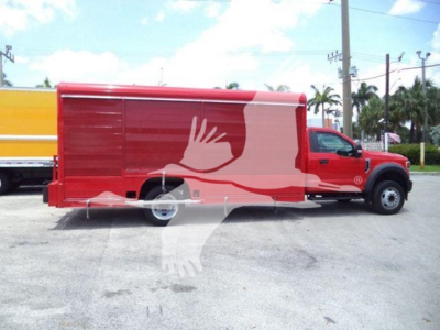 Ford F-550 van body in red side view with graphic white hand logo and beige cargo trailer, during daytime