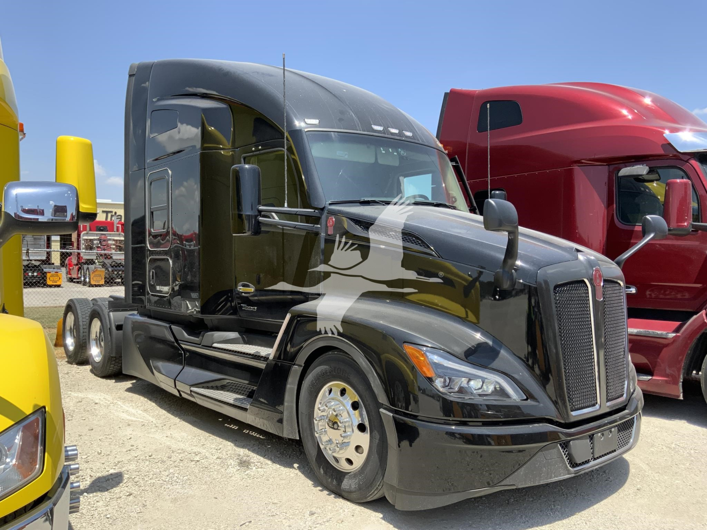 Kenworth T680 conventional sleeper truck in a used-truck lot side view, with glossy black paint and chrome grille; other trucks in background.