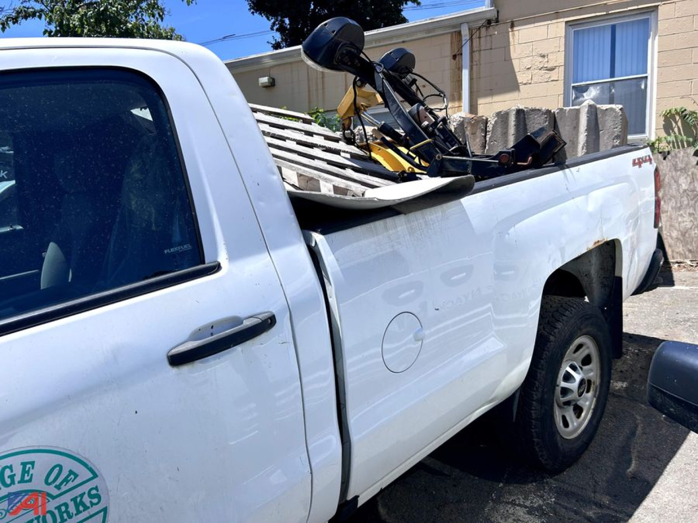 Side view of a white 2016 Chevrolet Silverado 3500HD pickup with a flatbed carrying a mounted snowmobile, showing door, rear wheel, and payload on bed.