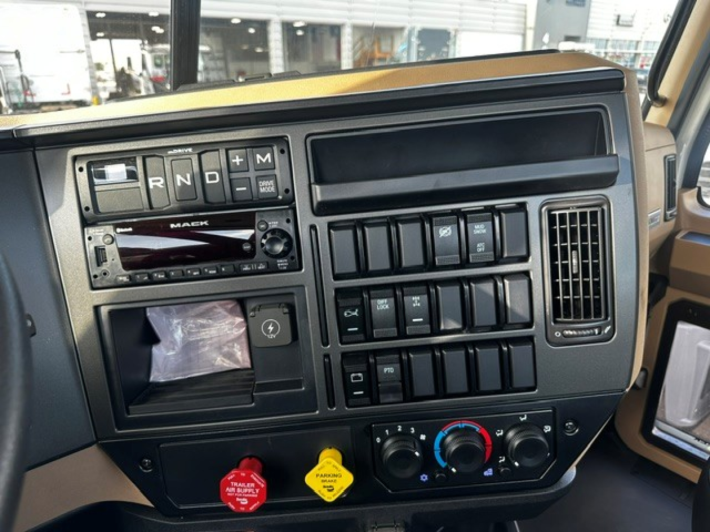 Truck cab interior dashboard showing gear shift selector (R N D P) and Mack stereo unit, numerous switches, climate controls, and warning indicators.