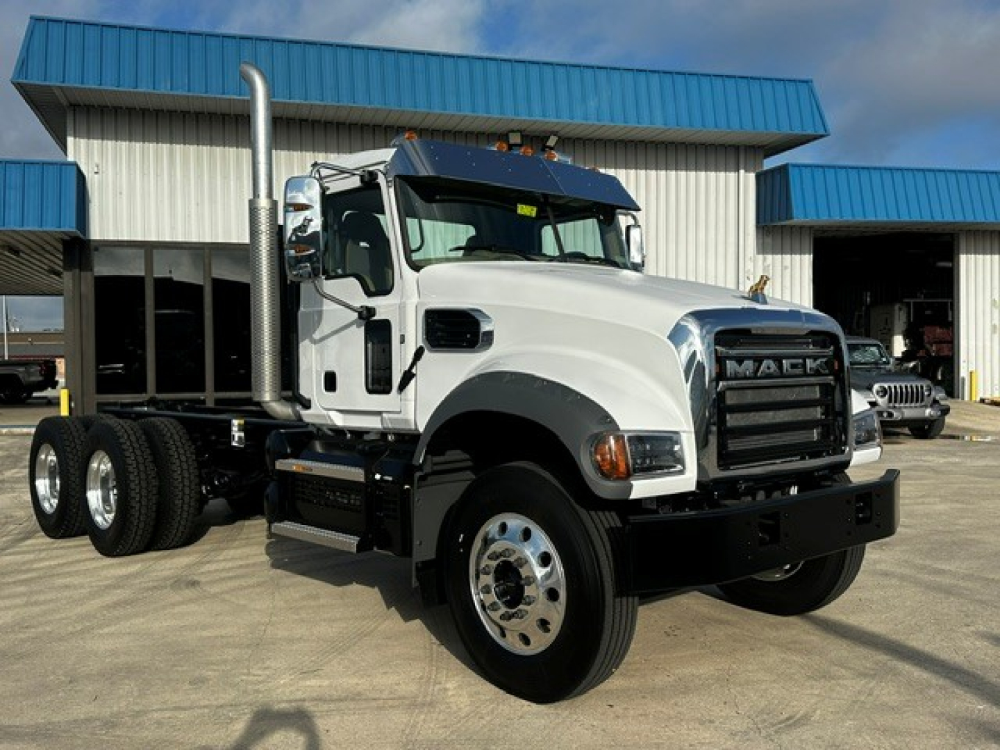 New 2027 Mack GR64F dump truck in white with dual rear axles and chrome grille, front view showing large exhaust stack and heavy-duty bumper.