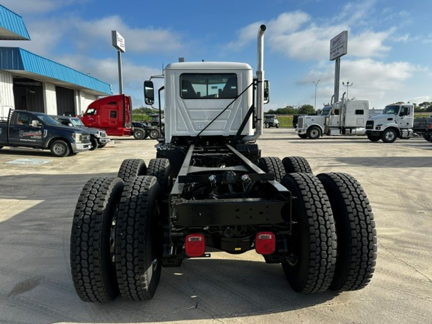 Mack GR64F truck chassis rear view showing dual rear axles and frame with spare space, cab in background, clear sky.