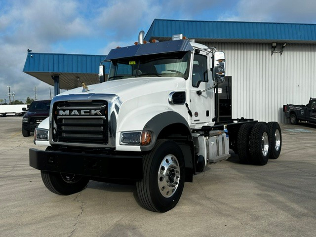 Mack GR64F dump truck in white with black grille, side view showing front and cab, twin rear axles, blue building in background.