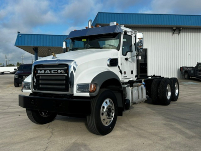 Mack GR64F dump truck in white with black grille, side view showing front and cab, twin rear axles, blue building in background.