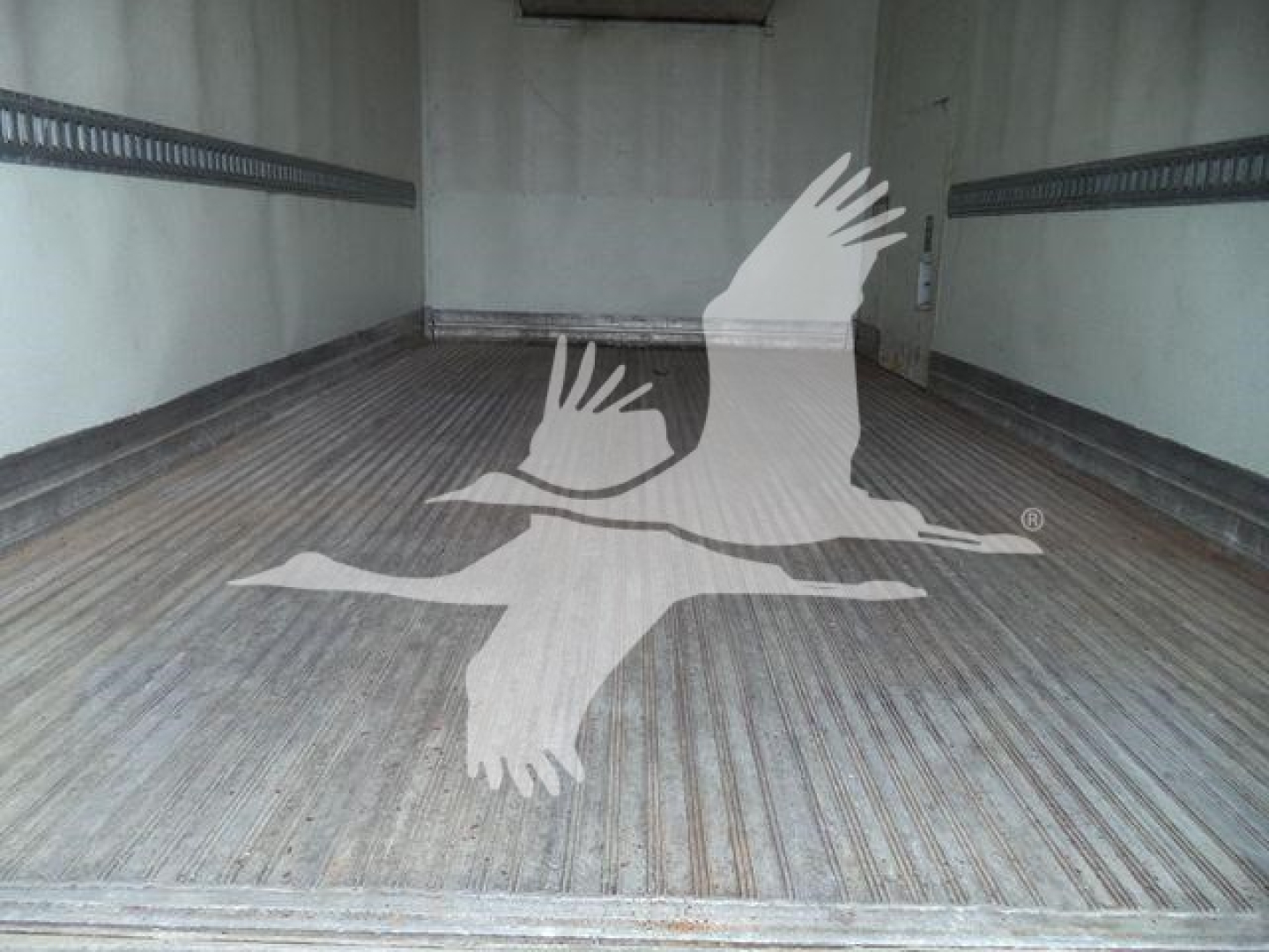 Interior of a refrigerated truck trailer with ribbed metal floor and tie-down rails along the walls.