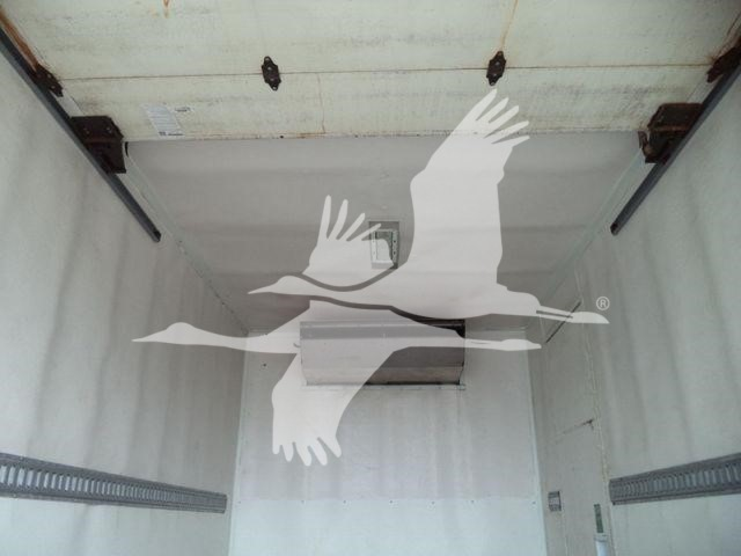 Interior of refrigerated truck cargo area with white silhouette of flying birds overlaying. No readable text visible on walls.