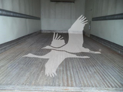 Interior of a refrigerated truck trailer with ribbed metal floor and tie-down rails along the walls.