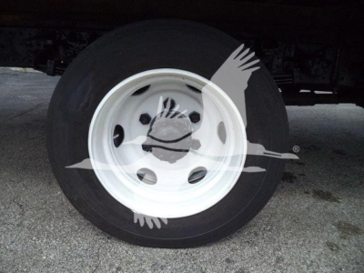 Wheel and tire of a refrigerated truck, white steel rim with vent holes; portion of undercarriage visible.