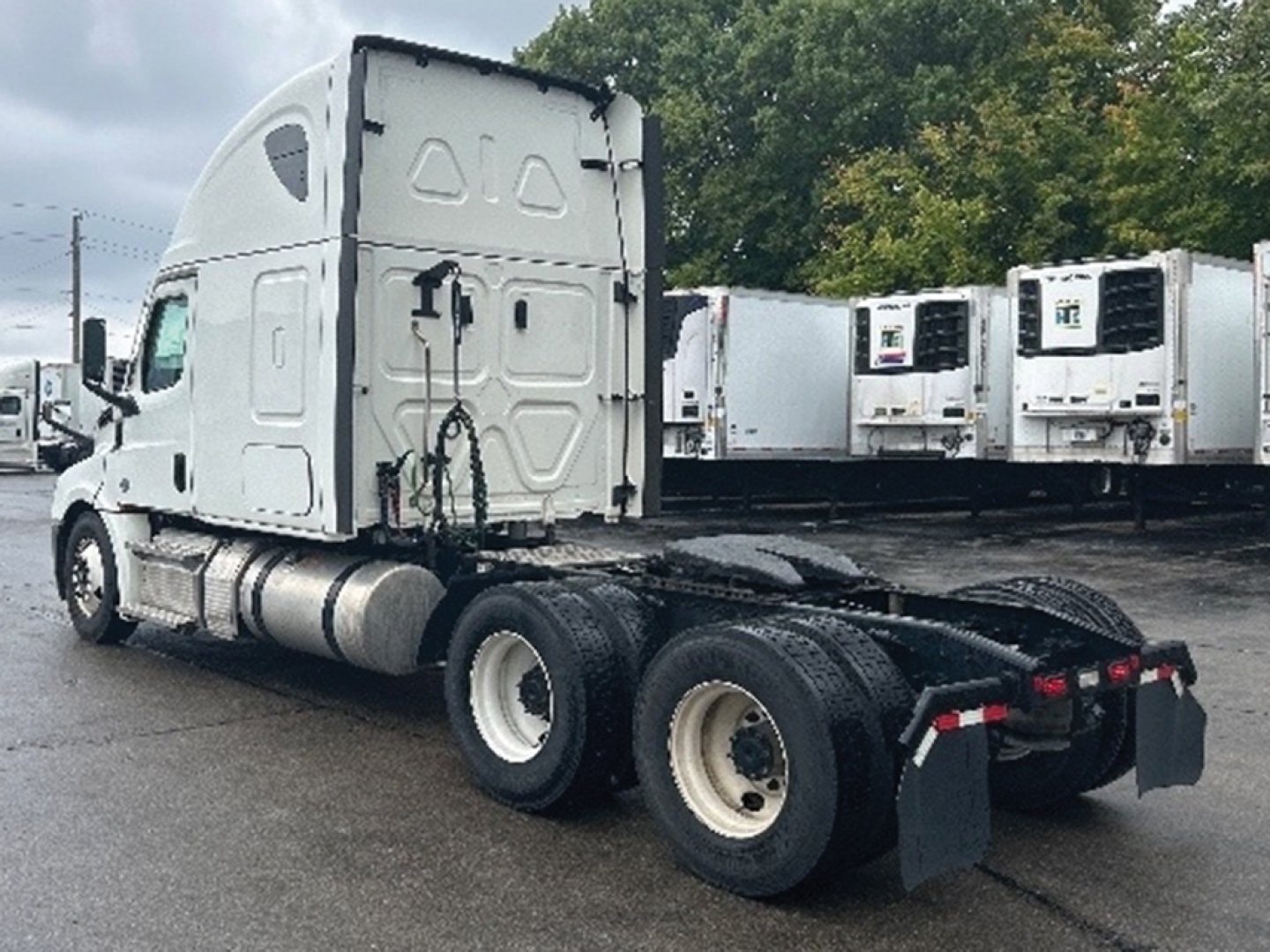 Truck tractor from rear-left side showing fifth wheel and dual rear axles with white fuel tanks and sleeper cab.