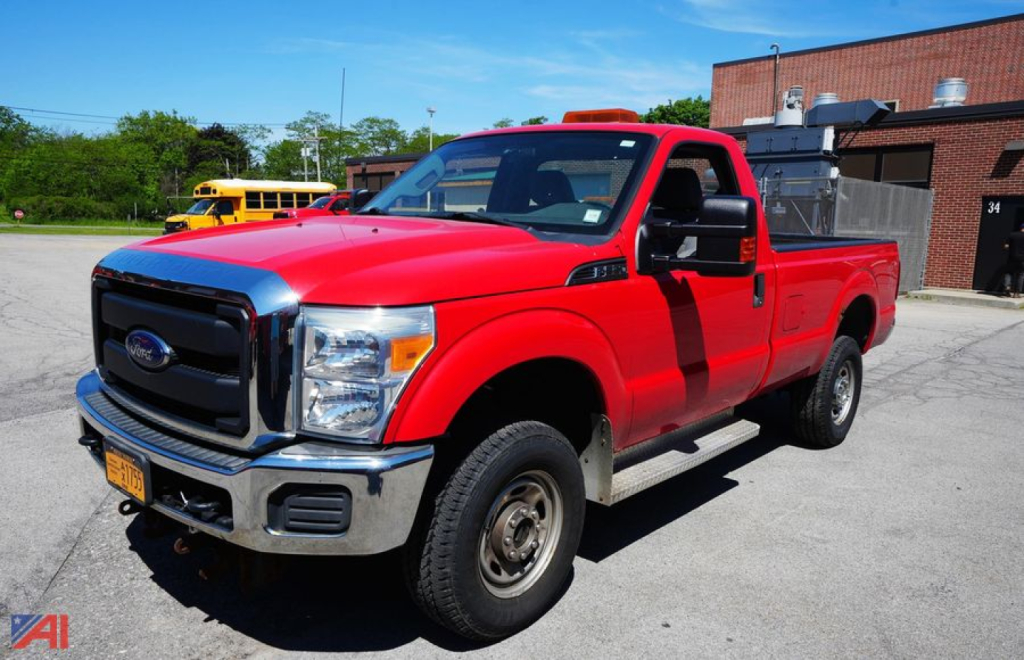 Ford F-350 XL SD dually pickup truck with plow in red, front-left view, cargo bed visible, orange emergency light bar on cab roof.
