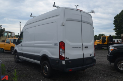 Ford Transit high-roof cargo van in a used condition, rear view showing back doors and taillights, with other trucks in background.