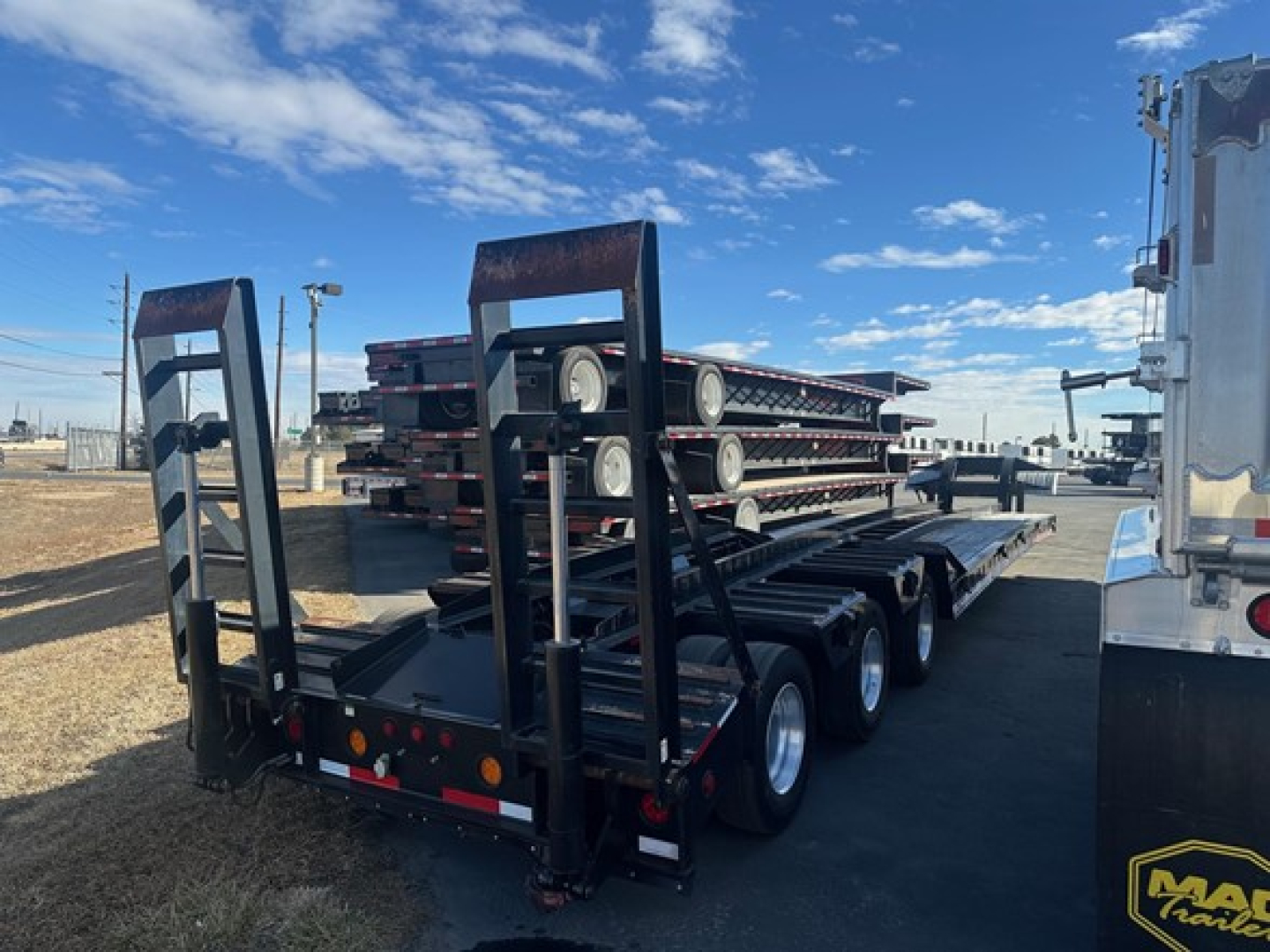 Trailer with multiple steel beams and wheels on a lowboy trailer, stacked perforated metal frames, rear ramps, and wheel chocks visible.