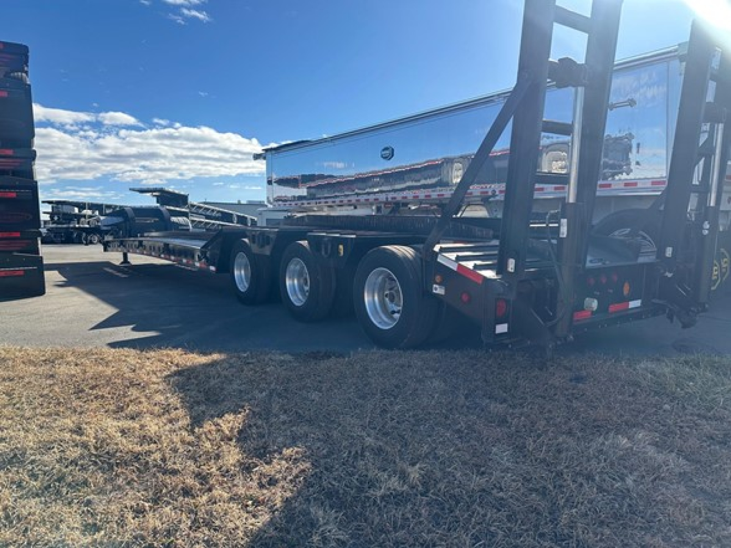 Trailer: Kalyn Siebert lowboy with multiple axles and chrome polished surface, side view showing tandem axle wheels and rear forklift rack.