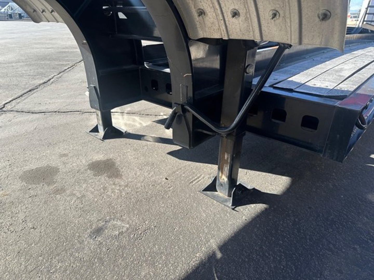 Kalyn Siebert lowboy trailer underside showing support legs and frame components with hydraulic lines and mounting brackets.
