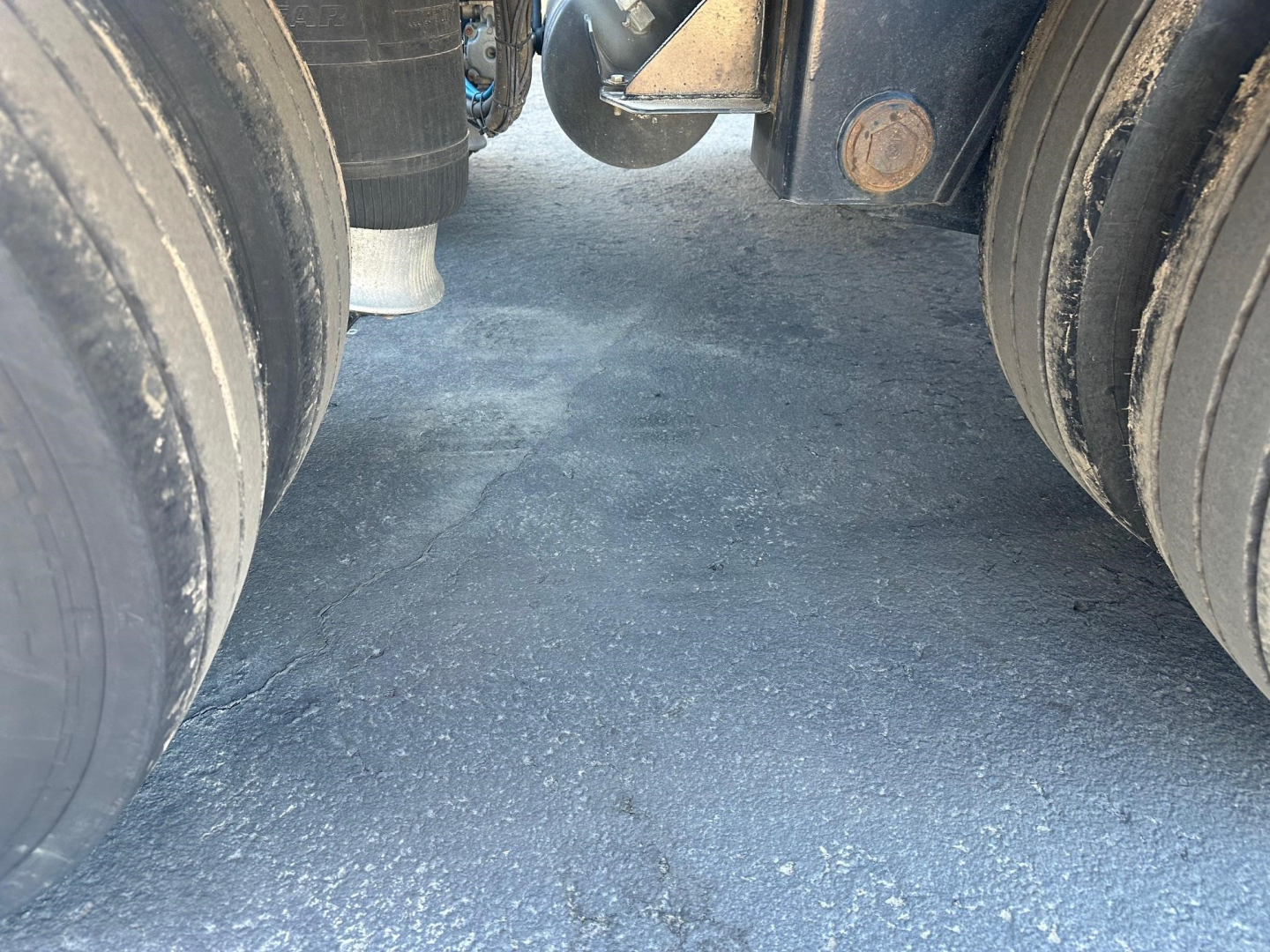 Kalyn Siebert lowboy trailer underside between dual rear axles showing trailer suspension and ground surface.