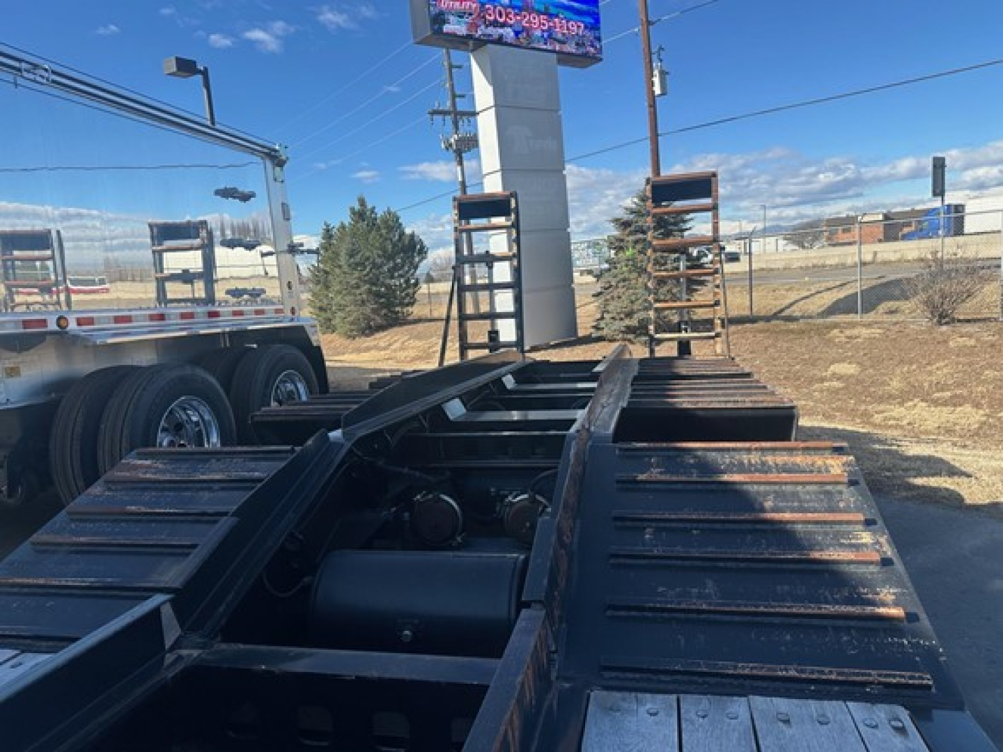 Lowboy trailer chassis showing exposed frame rails and hitch area with support brackets and dual rear axles visible at the back.