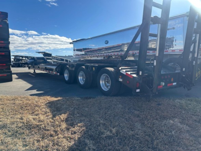 Trailer showing triple-axle beaver tail lowboy with silver polished side rails and hydraulic forklift attachment at rear.