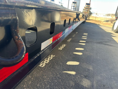 Trailer side rail with cutouts and reflective red-white-yellow stickers along the length, lowboy trailer style.