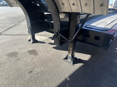 Trailer undercarriage showing support legs, mounting brackets, and hydraulic lines; metal frame and curved wheel arch visible with bolted joints.