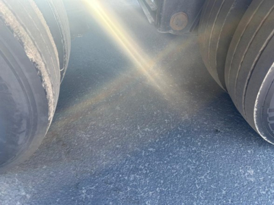 Kalyn Siebert lowboy trailer wheel area showing dual air springs and tires with sunlight glare on asphalt.