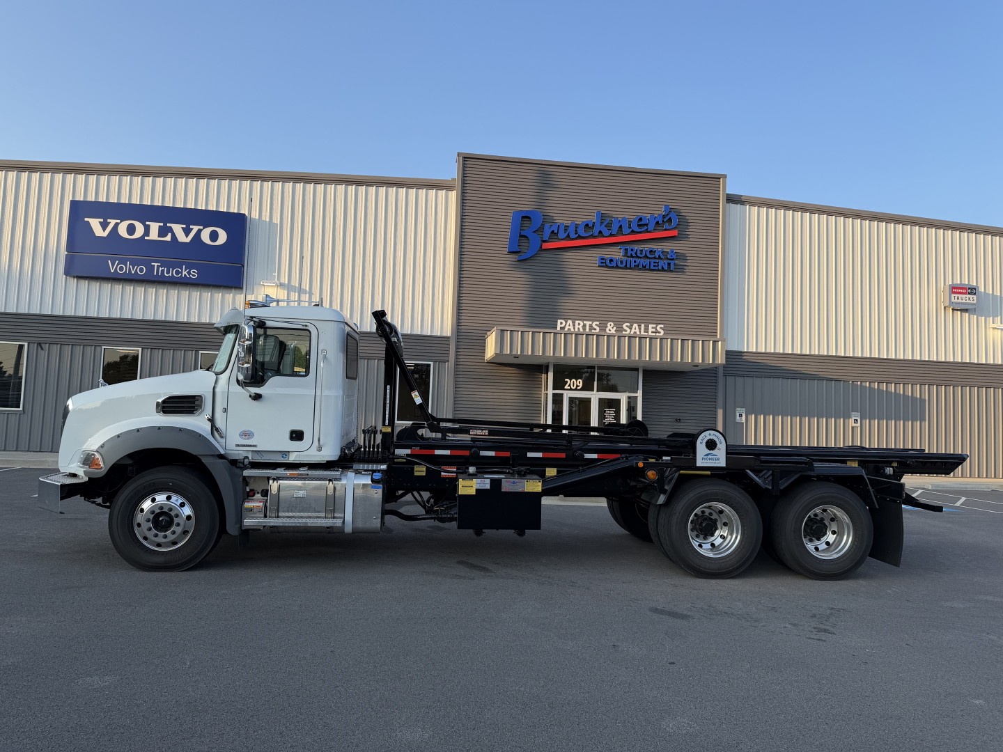 New Mack GR64B roll-off truck on lot in front of building with Volvo Trucks sign and Buckner's Trucks Equipment signage.