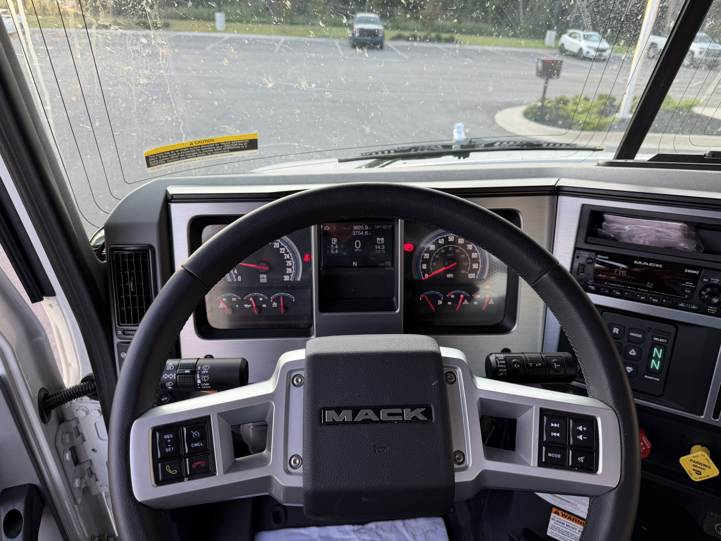 Mack GR64B truck cab interior showing steering wheel with Mack logo, instrument cluster, and dashboard controls.