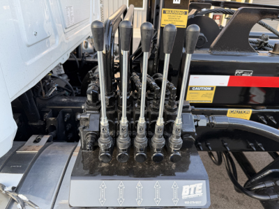 Control levers and hydraulic control manifold on Mack GR64B roll-off truck showing multiple black handles and label area.