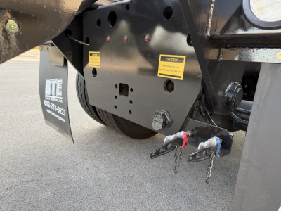 Mack GR64B rear view showing hitch pins and warning labels on the frame, black undercarriage with yellow caution stickers.