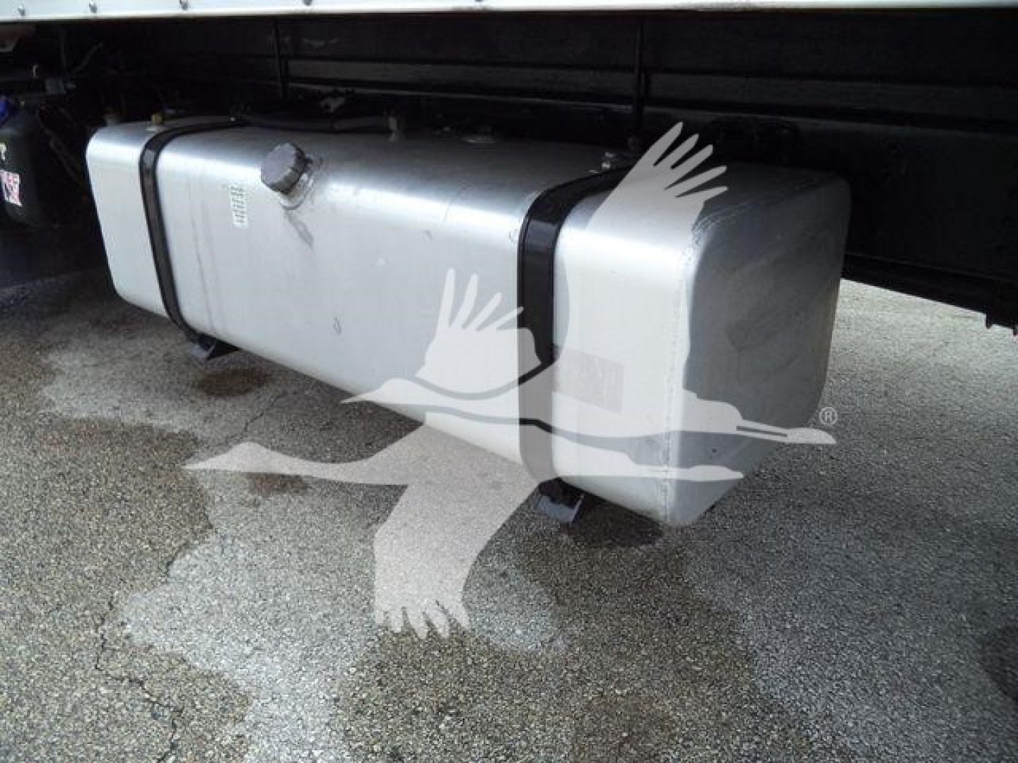 Isuzu box truck undercarriage showing a rectangular aluminum fuel tank or auxiliary tank with two black straps; writing on tank appears blurred.