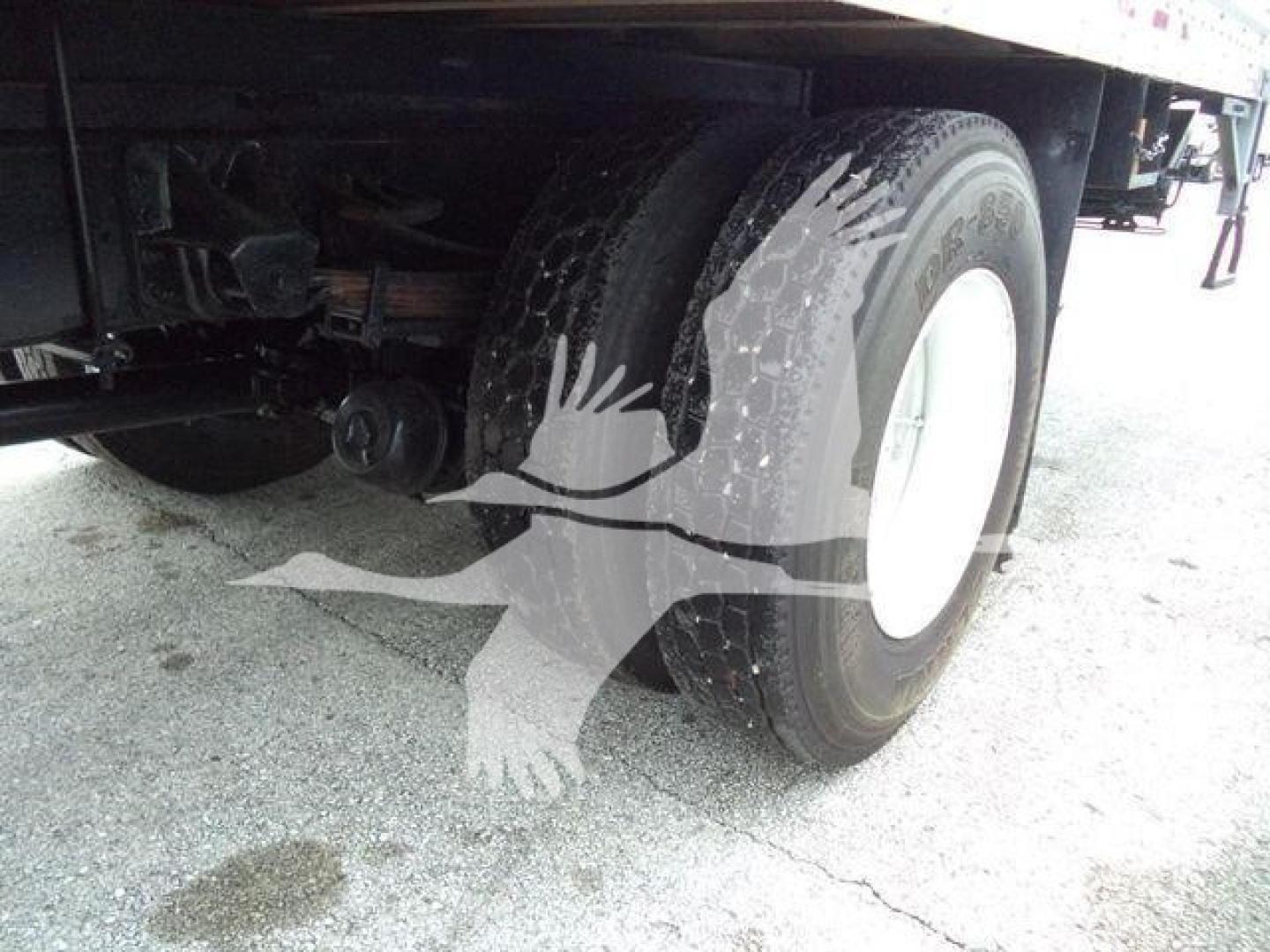 Truck wheel and undercarriage view showing rear dual tires, suspension, and part of frame.