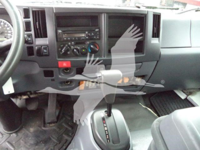 Isuzu NPR/Box truck dashboard and gear selector area with steering wheel on left; central console shows radio and climate controls; gear shift visible near floor.