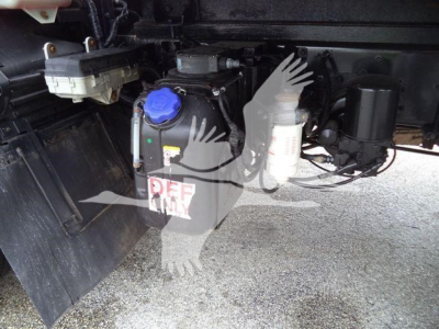 Isuzu truck undercarriage showing coolant reservoir with blue cap and DEF container, hoses and wiring visible.