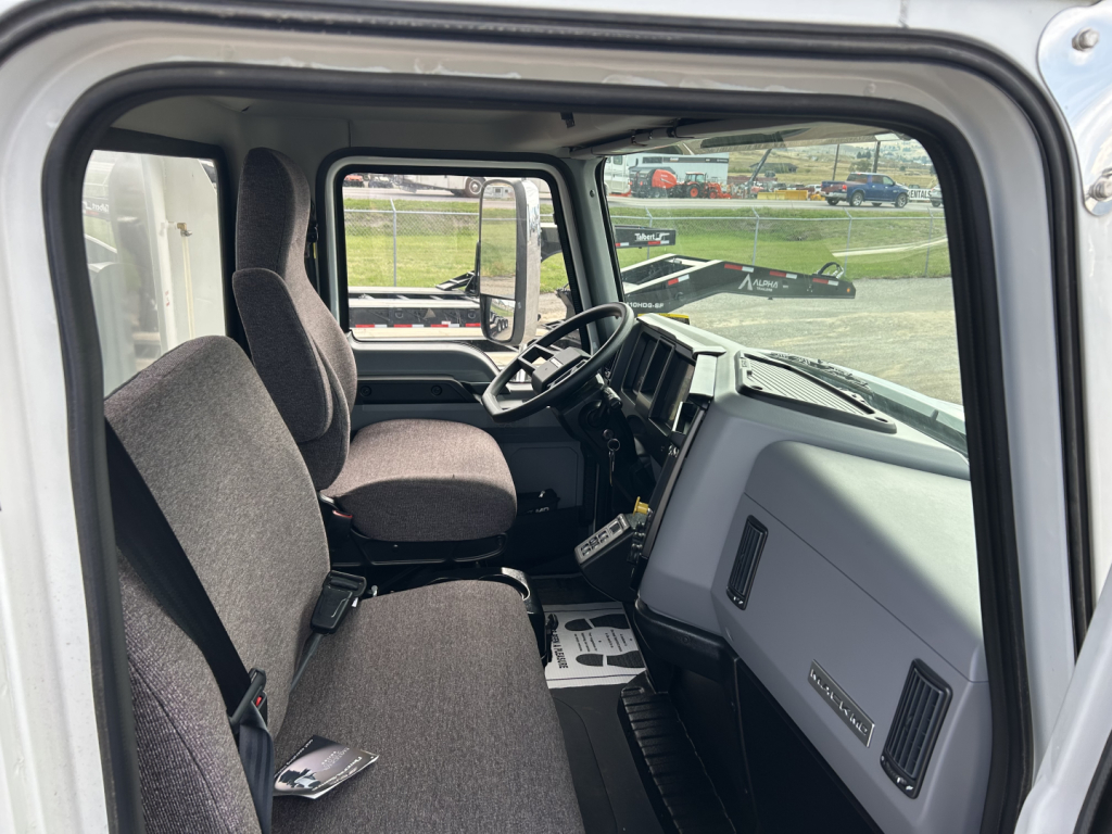 Cab interior of a new 2025 Mack MD7 truck showing two front seats, steering wheel, dashboard, and center console.
