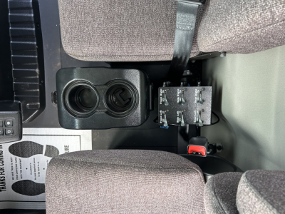 Dashboard area showing cup holders and switch panel inside a Mack MD7 cab; two circular cupholder recesses and a small electronic switch panel with toggle switches visible.