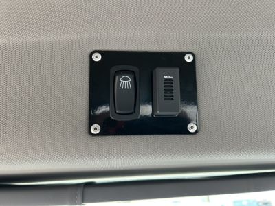 Trucks cab interior panel with two switches: a circular light/switch and a MIC microphone panel, mounted on a dark plate with four screws.