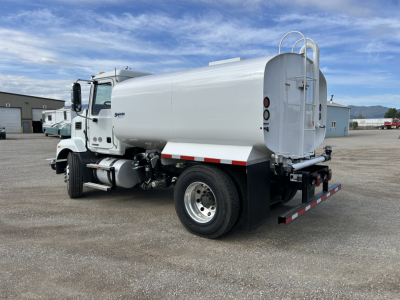 Side view of a white 2025 Mack MD7 water tanker truck with cylindrical tank, rear access ladder, and dual rear wheels, showing brand text on cab and rear bumper.