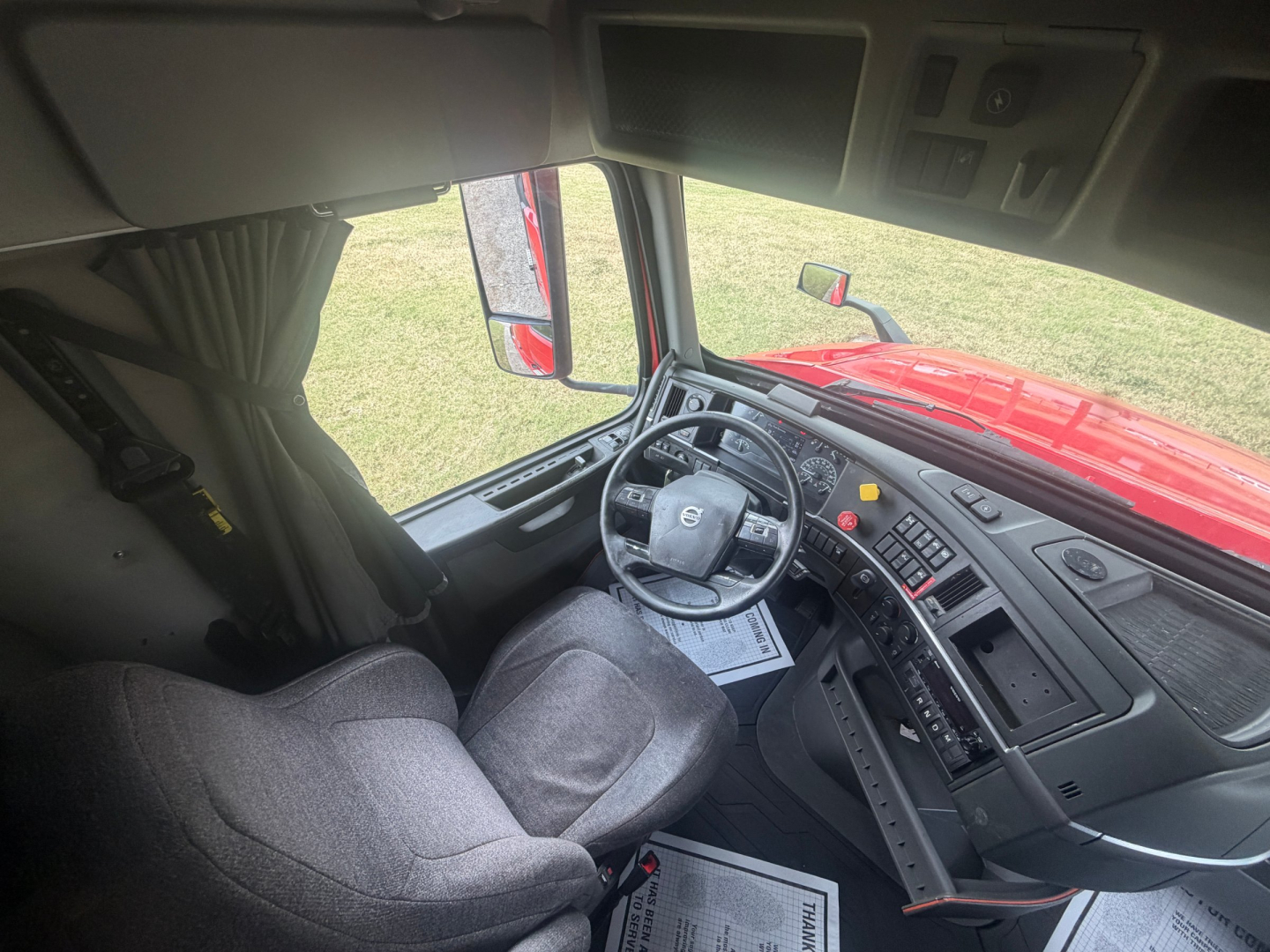 Volvo truck cab interior showing steering wheel with Volvo logo, dashboard controls, and driver seat.